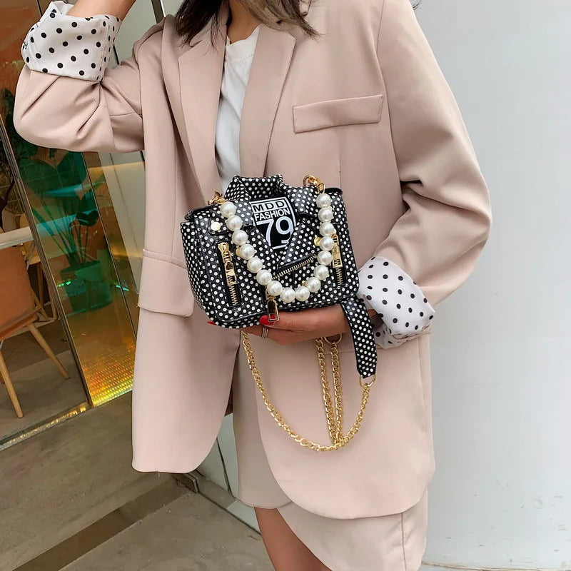Person holding a polka dot handbag with pearl embellishments and a gold chain.