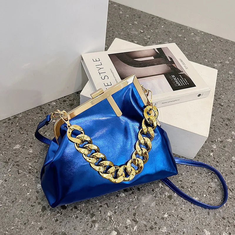 blue Carauana UNIU Aurora Clutch with gold chain detail on a gray surface