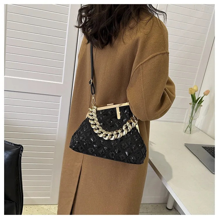 Person holding a black handbag with gold chain detail in an indoor setting.