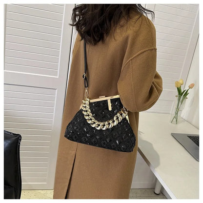 Person holding a black handbag with gold chain detail in an indoor setting.