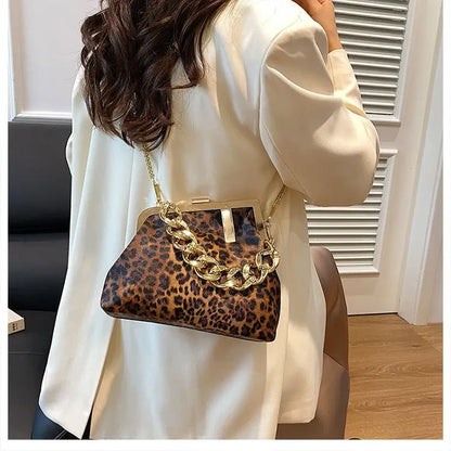 Person wearing a white coat holding a Carauana_UNIU_Leopard_Clutch with a gold chain strap.