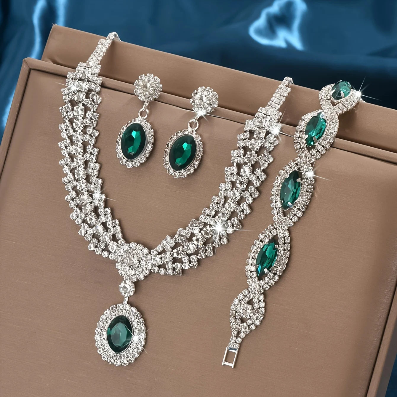 Jewelry set with necklace, earrings, and bracelet featuring green gemstones on a brown surface.