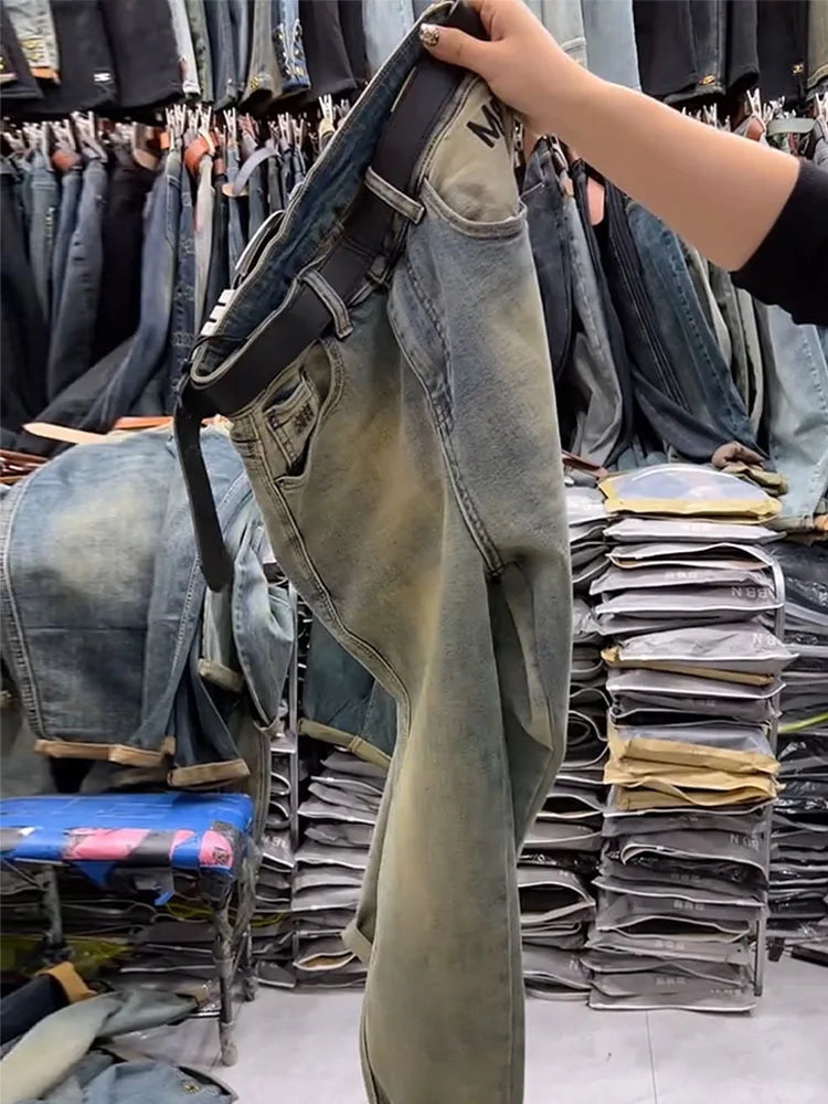 Person holding a pair of jeans in a clothing store with stacks of jeans in the background.
